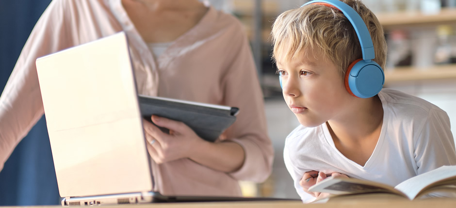 Un jeune garçon fait ses devoirs sur un ordinateur sécurisé avec sa mère en arrière-plan