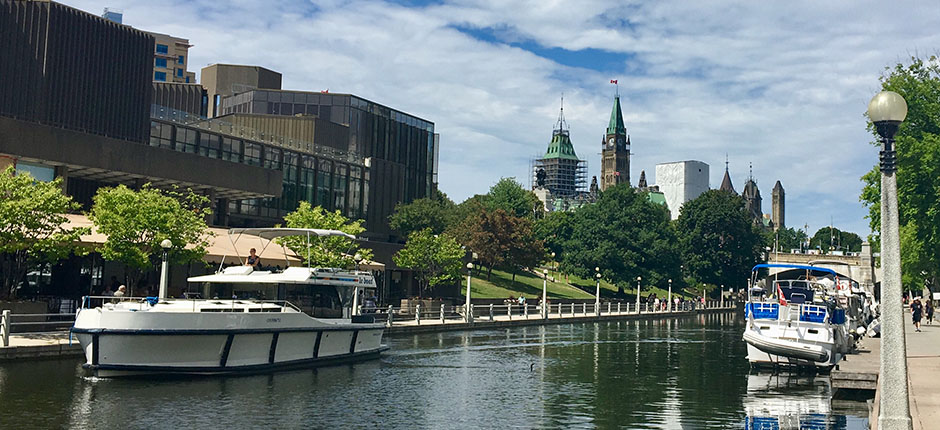 Boats docked along the canal in Ottawa with the parliament buildings in the distance.