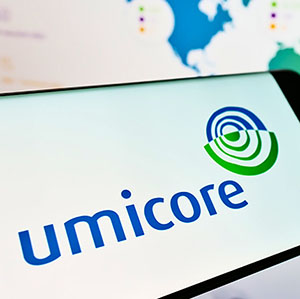 A cell phone displaying the Umicore logo in front of a computer showing a map of company locations.