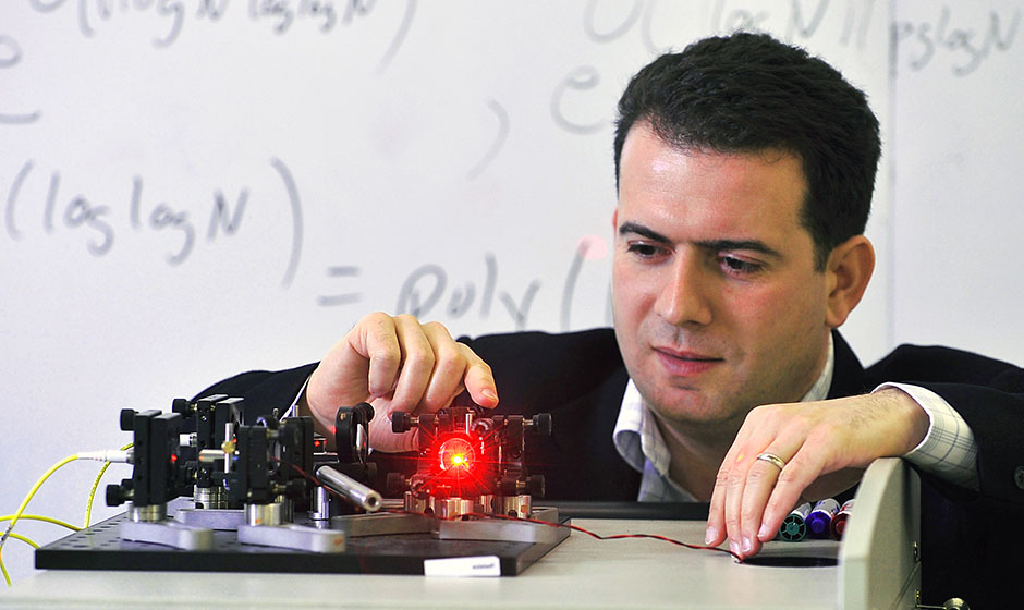 Dr. Michele Mosca is working on a small device on a tabletop that is connected by wires and has a shining red light.