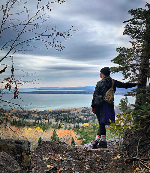 Hiker leaning against a tree, looking out at a vista of the great lake from a higher elevation.