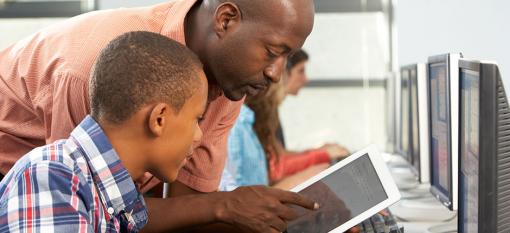 A cybersecurity instructor helping a school age boy use a tablet securely