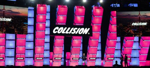 Collision main stage with pink and purple light-up pillars and an enthusiastic host gesturing to the audience